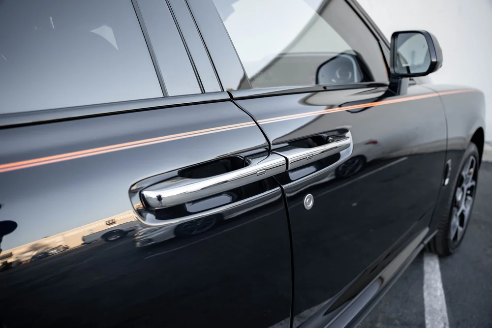 Black Rolls-Royce Cullinan Black Badge — paired door handles, dark body-panel reflections and orange coachline
