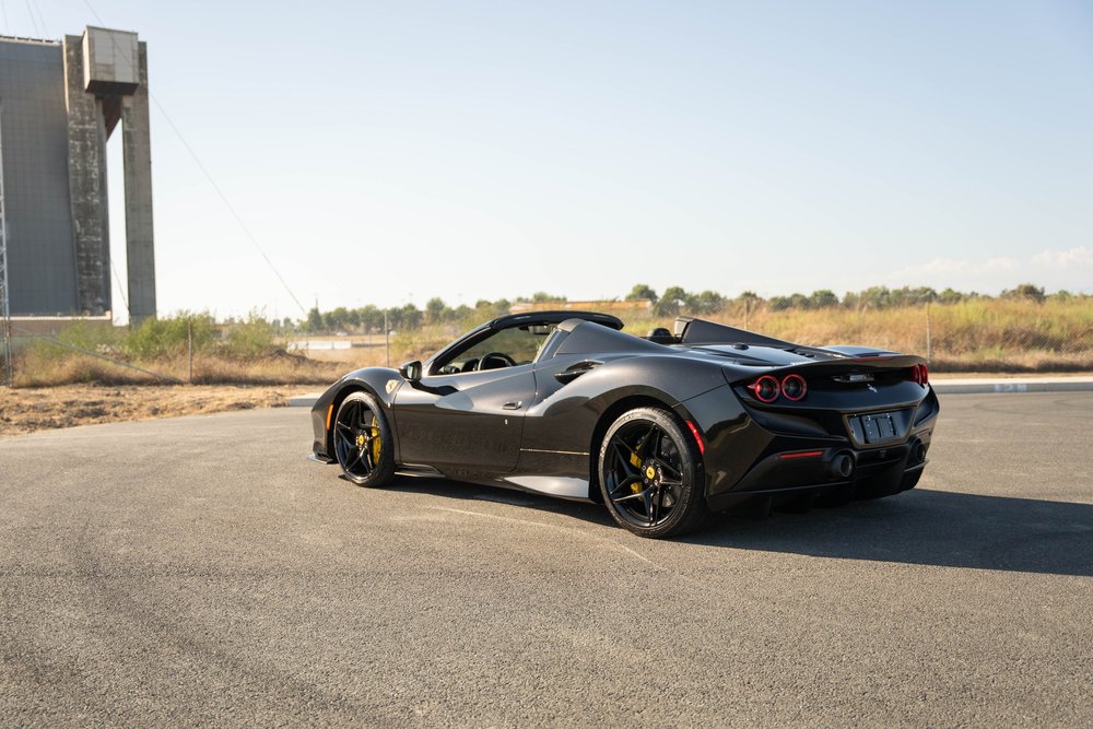 Complete rear three-quarter view of the black Ferrari F8 showing open cockpit and yellow brake calipers