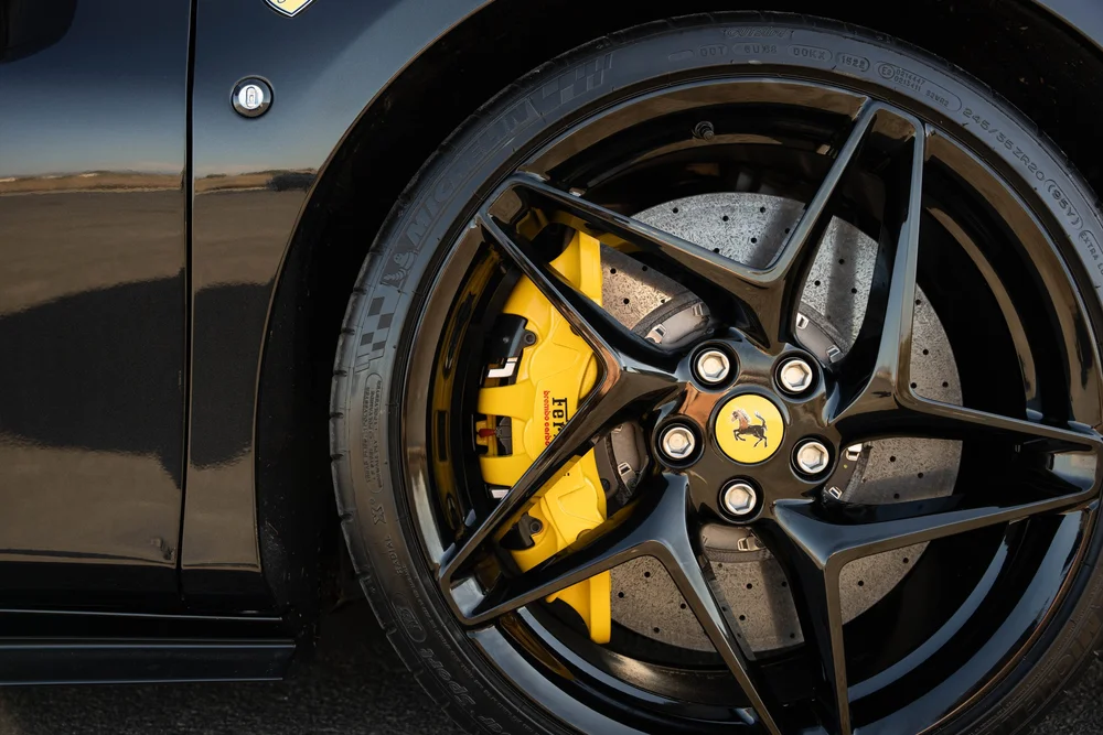 Black Ferrari F8 wheel close-up with black spokes, yellow brake caliper and drilled brake disc