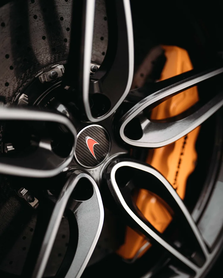 Red McLaren wheel-center emblem surrounded by dark spokes with an orange caliper behind.