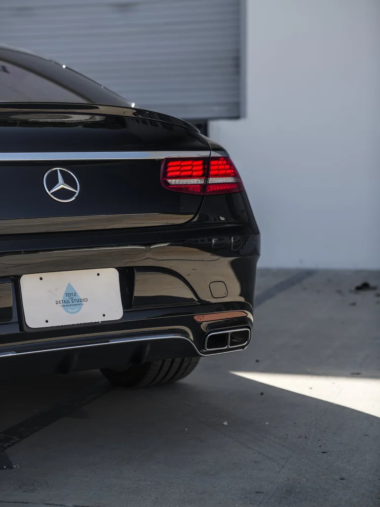 Close rear-corner view of the black Mercedes-Benz S 560 with a red taillight, Mercedes star, white Toyz plate and paired rectangular exhaust outlets.