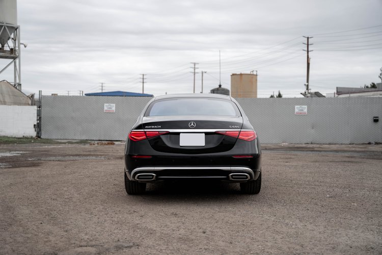 Complete straight rear view of the black Maybach with both red lamps and bright exhaust surrounds across a broad gravel foreground