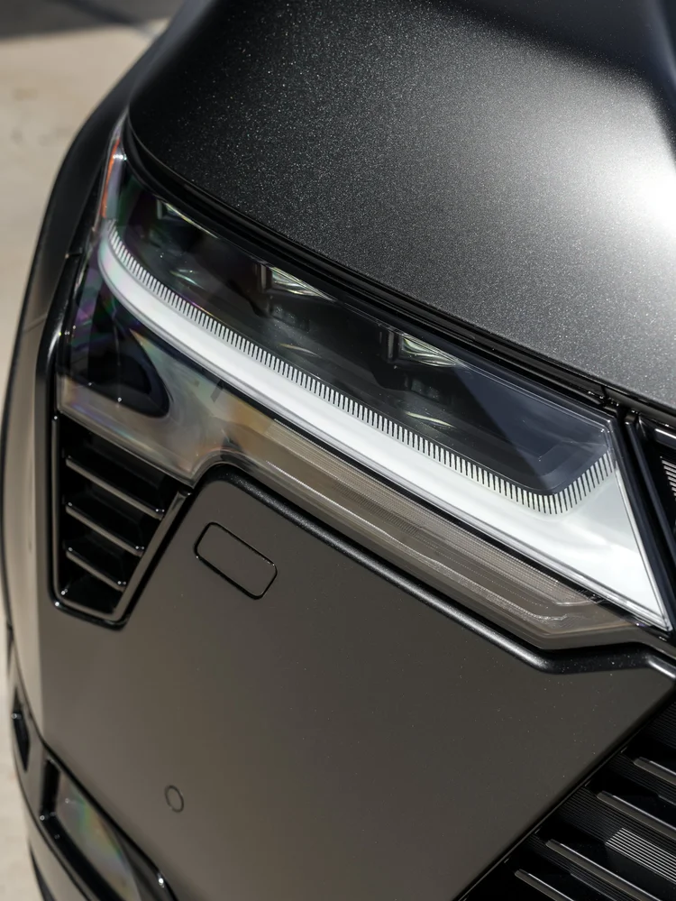 Angled close view of an illuminated GX 550 headlamp beneath a dark matte-looking hood edge with a white light strip and amber outer element