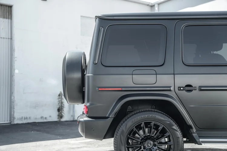 Rear side-body detail of the grey G 550 with dark glass, a fuel door, red trim reflector and black rear wheel