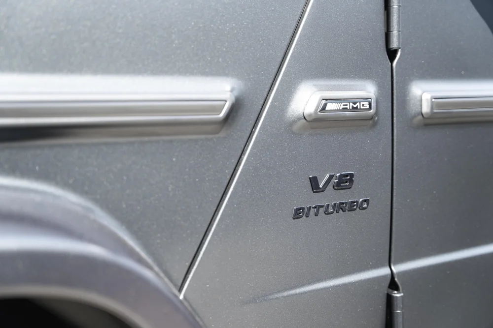 Close-up of the AMG plaque and V8 BITURBO lettering on the matte-looking grey fender beside a black door hinge