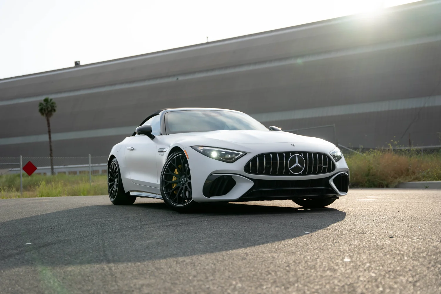 Complete front-three-quarter landscape of the white Mercedes-AMG SL 63 with lit headlamps, dark wheels and yellow calipers on pavement