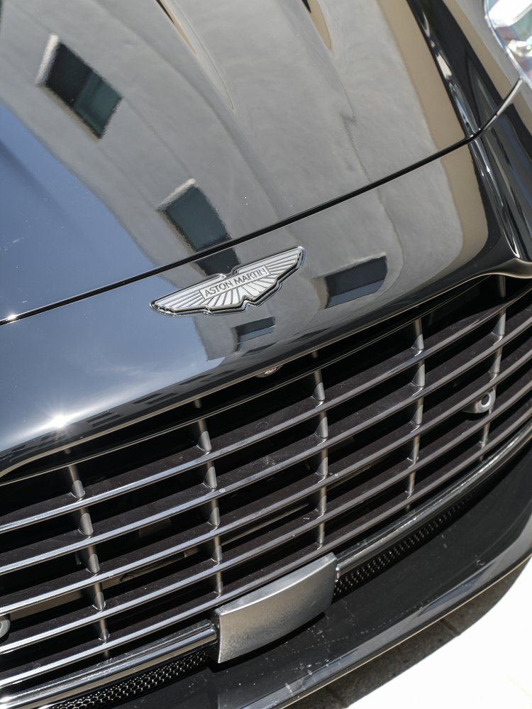 Aston Martin wing badge above the DB12 front grille on reflective black bodywork.