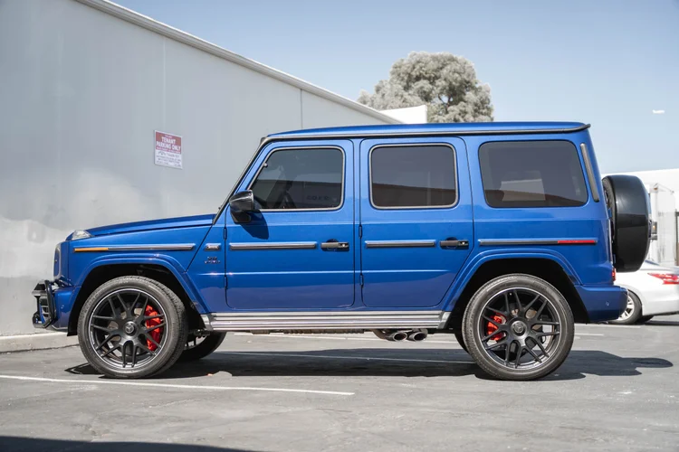 Complete side profile of the blue G 63 with dark silver-edged wheels, red calipers, silver running boards and twin side exhaust tips