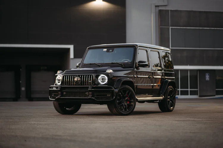 Dark Mercedes-AMG G 63 from the front three-quarter angle, with bright circular headlamp rings, black wheels and a running board.
