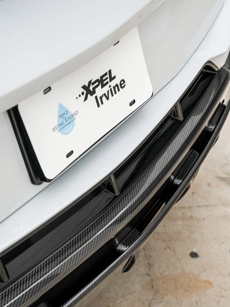 Rear display plate with Toyz Detail Studio and XPEL Irvine lettering above dark woven-pattern diffuser trim.