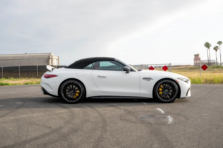 Complete side profile of the white SL 63 showing its dark fabric roof, raised rear spoiler and yellow calipers behind dark wheels