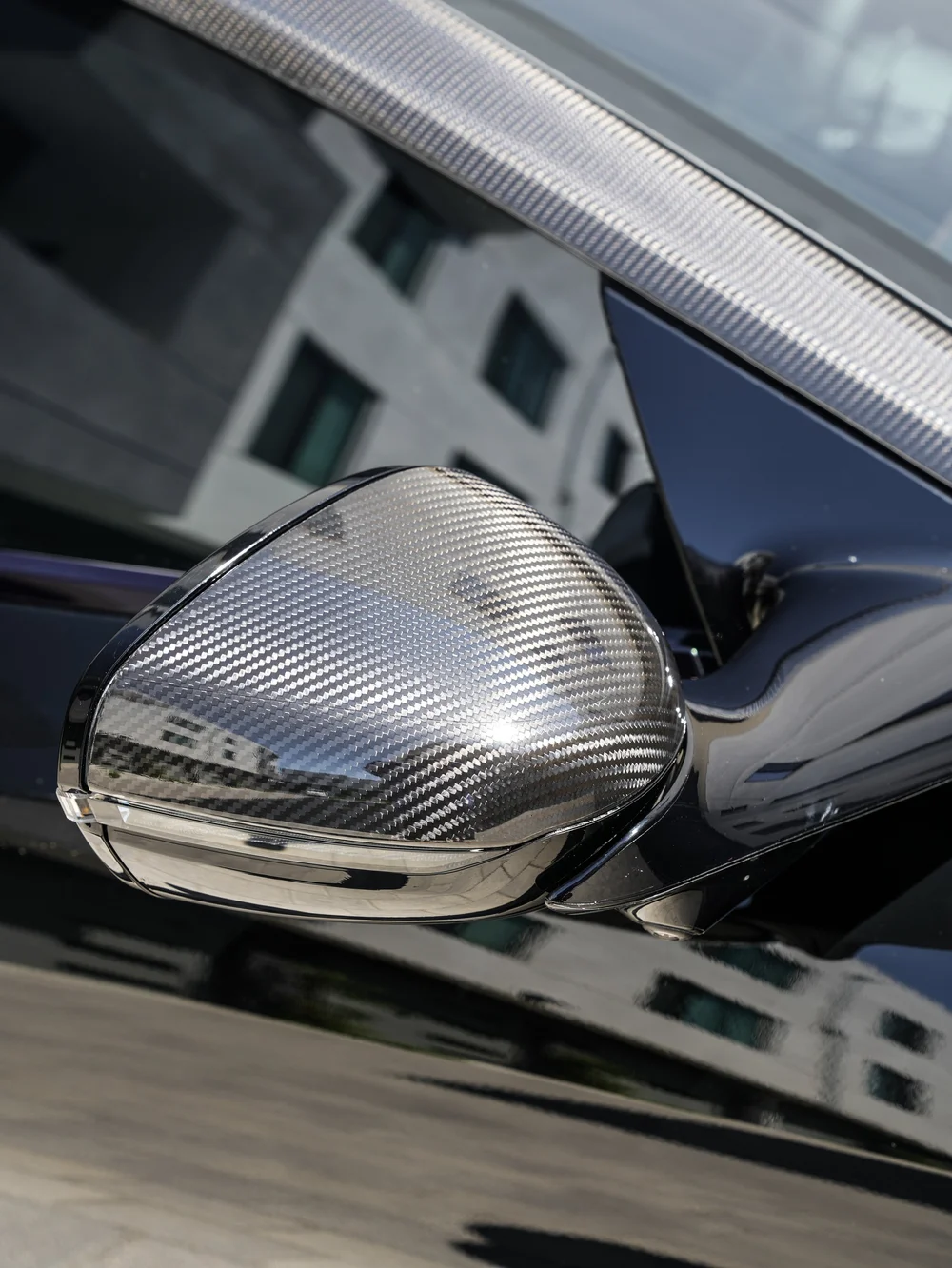 DB12 exterior mirror with a weave-pattern cap beside reflective side glass.