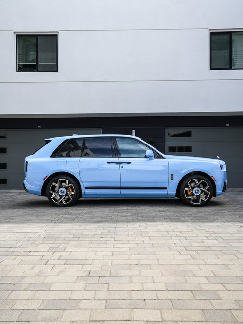 Light-blue Rolls-Royce Cullinan in a full side profile with dark side glass, two-tone wheels and gold-colored brake calipers