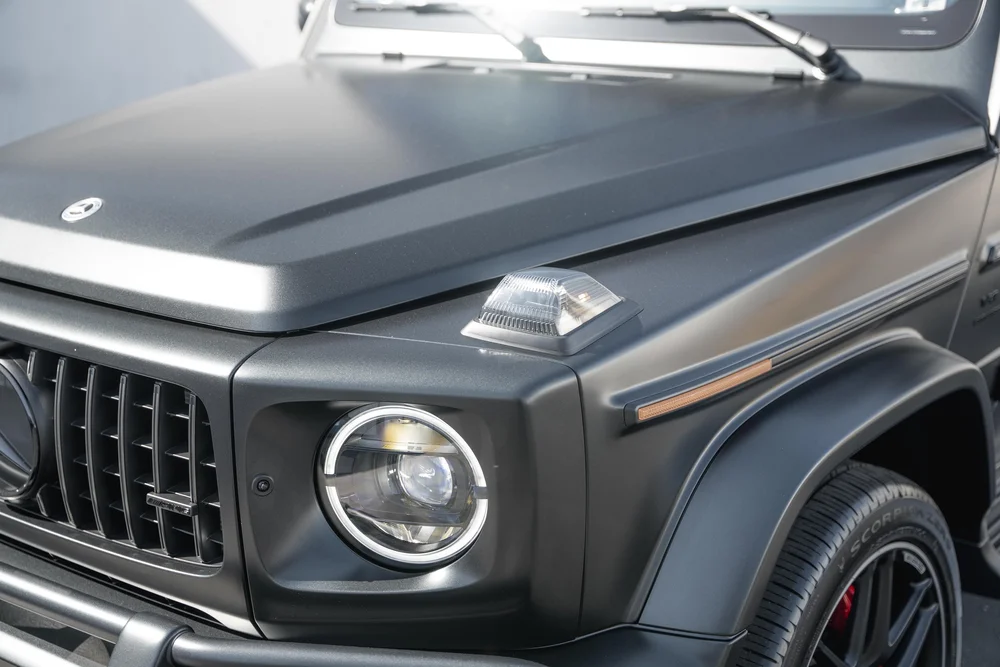 Grey G 63 front-corner detail with a clear fender-top lamp, circular headlamp, hood crease and dark wheel arch