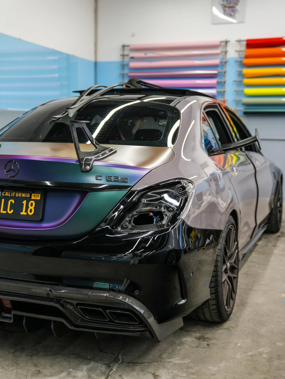 Indoor rear-quarter view of the C 63 S during wrap work, with mixed-color panels, loose material and an open rear lamp recess