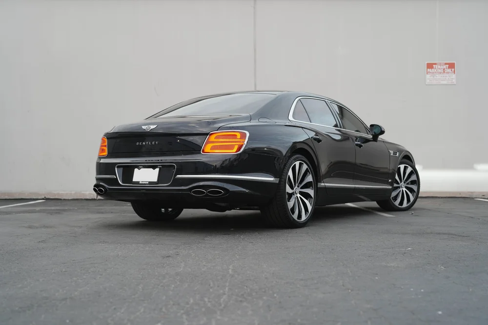 Dark sedan viewed from the rear corner with illuminated tail lamps.