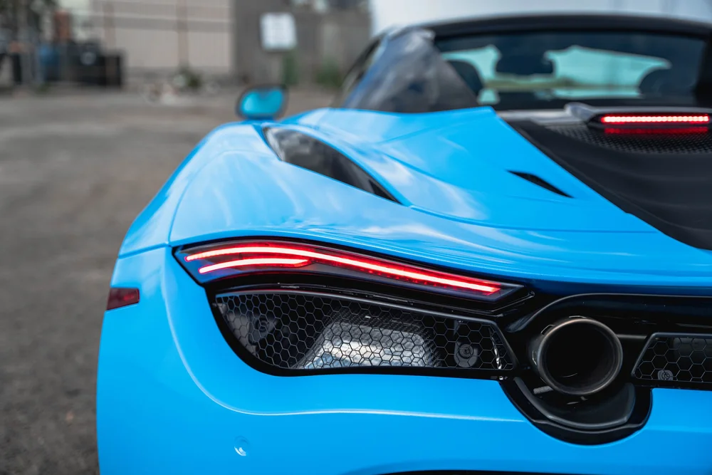 Close view of the 720S red taillight, rear mesh and round exhaust outlet framed by blue bodywork