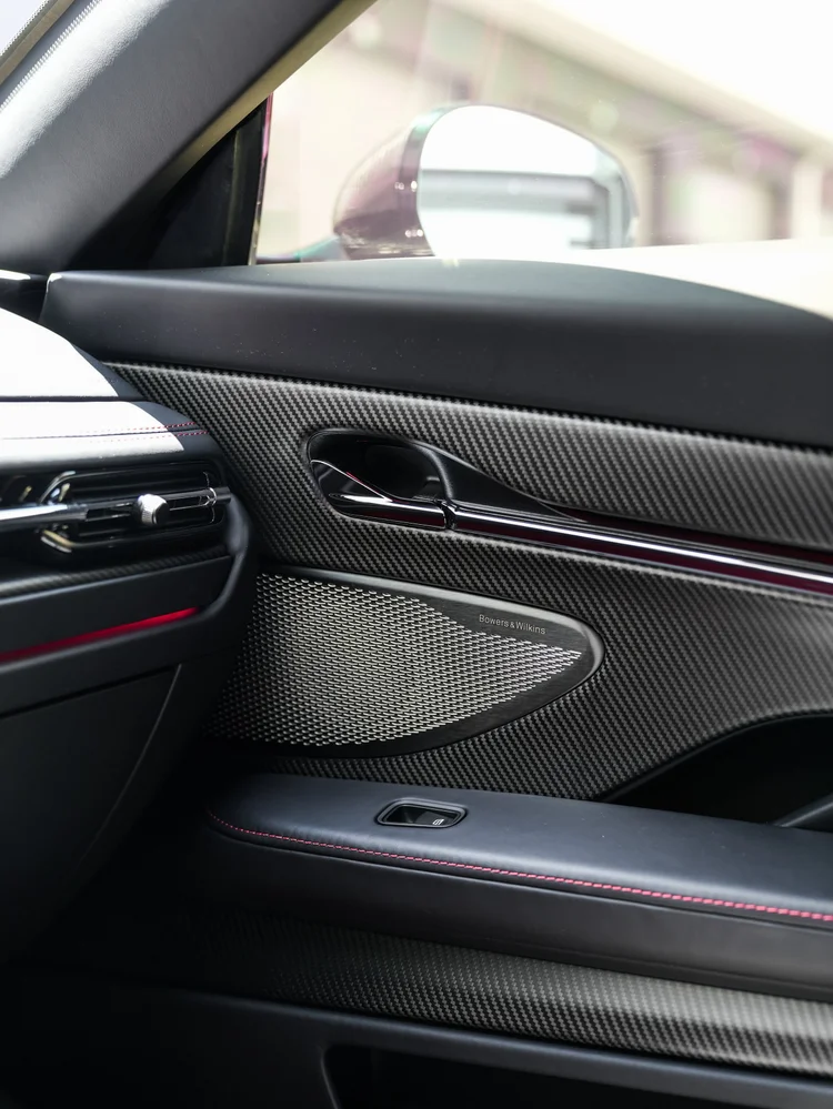 DB12 interior door panel with weave-pattern trim, handle, speaker grille and red stitching.