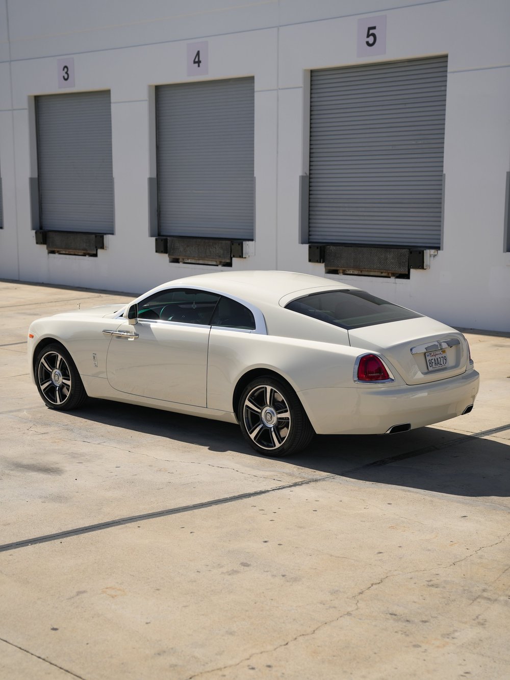 Complete rear three-quarter view of the pale Rolls-Royce Wraith with both wheels, red taillamps and exhaust openings.