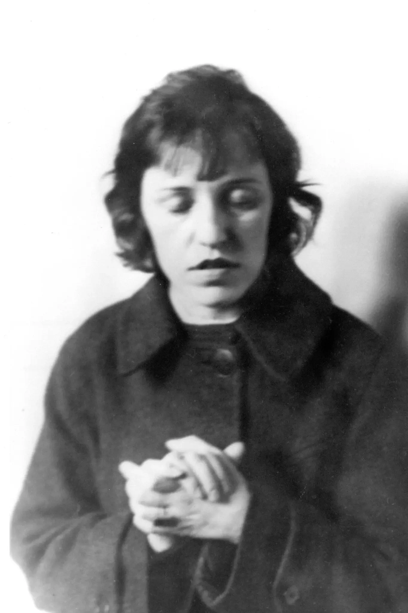 Black and white photograph of Austrian-American singer, diseuse, and actress Lotte Lenya, performing as the blind girl from “Das Lied vom weißen Käse” (Weill/Weisenborn). She dons short, dark hair, wearing a dark top, holding her hands together.