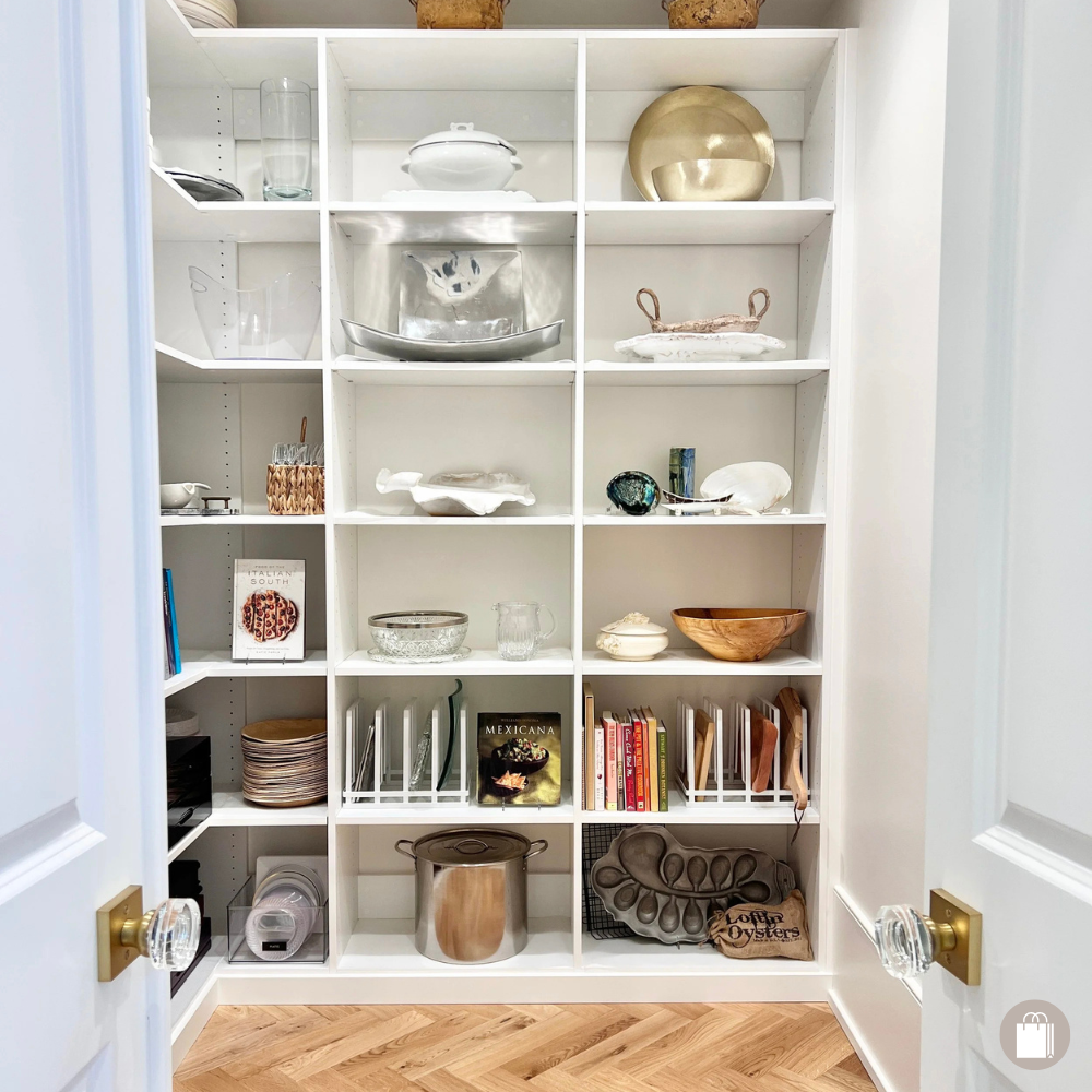 Organized pantry with white shelves featuring curated platters, cookbooks, oyster trays, and cookware, styled by Sorted Professional Organizing.