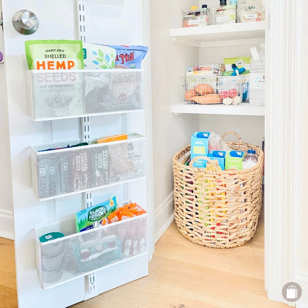 Elfa over-the-door utility track with white metal mesh baskets organizing snacks and a floor basket maximizing pantry space, arranged by Sorted Professional Organizing in New Orleans.