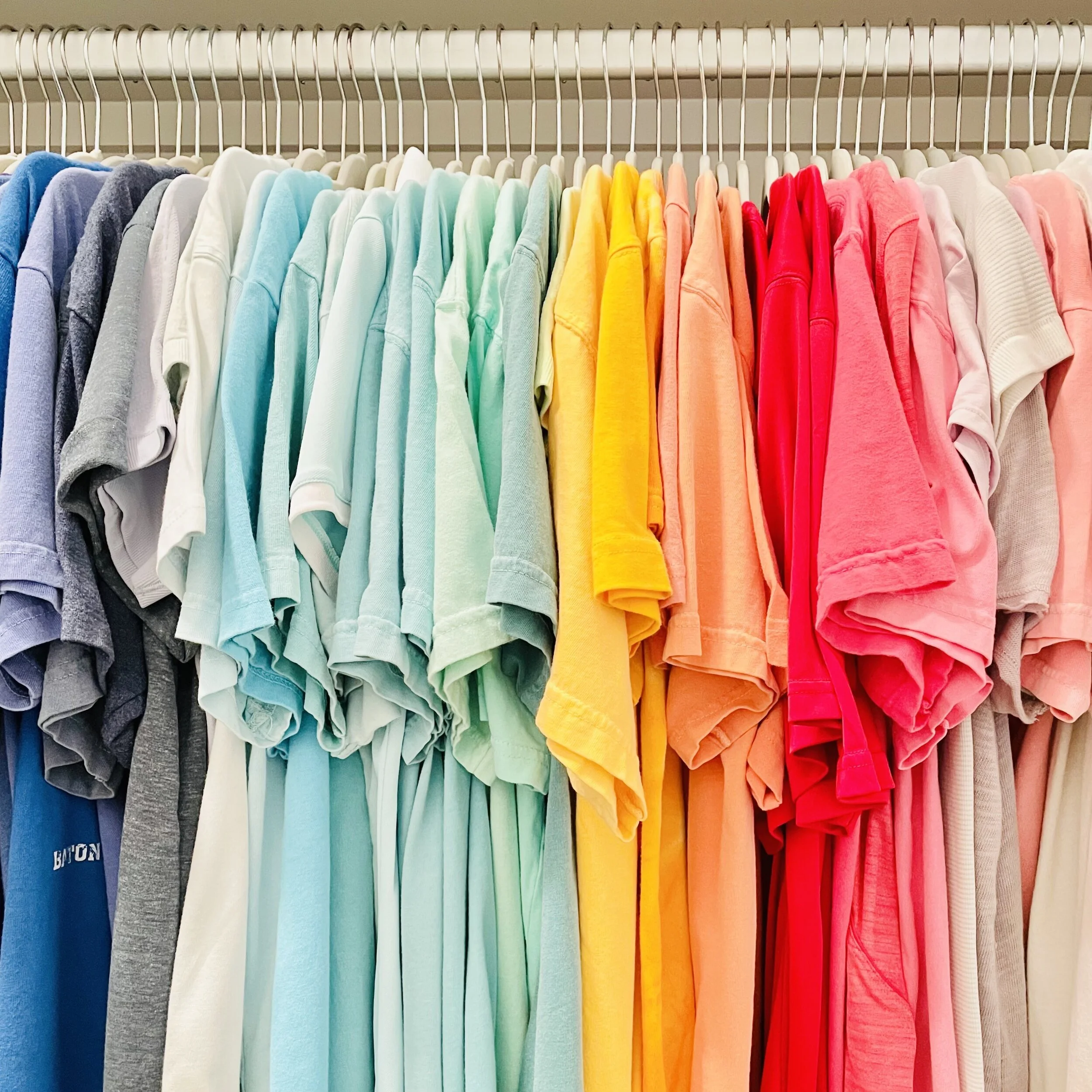 Color coordinated hanging shirts on ivory velvet hangers on a closet rack organized by Sorted Professional Organizing in New Orleans.