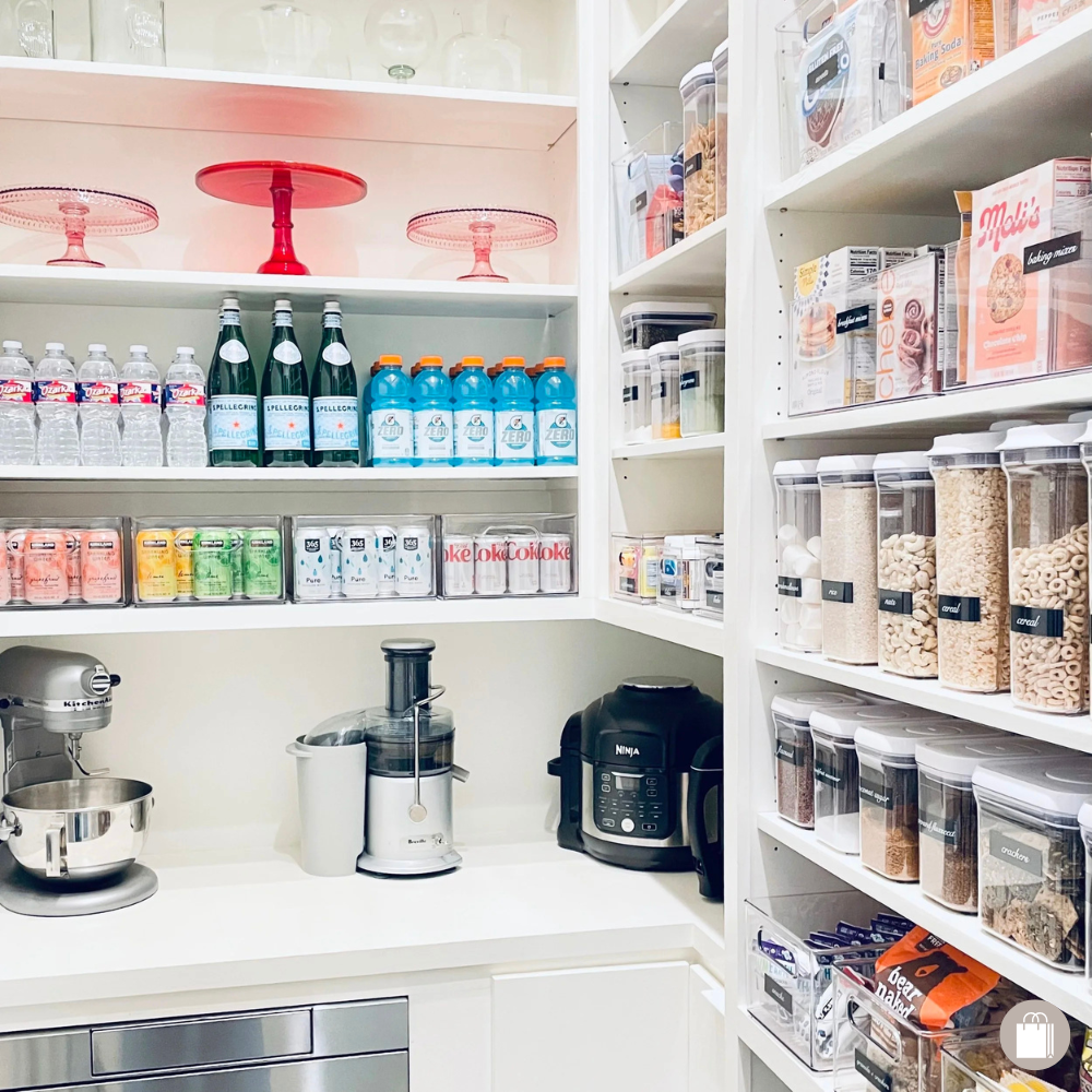 A gorgeous walk-in pantry with a variety of beverages, colorful cake stands, appliances, OXO dry food storage containers, and acrylic bins organized by Sorted Professional Organizing in New Orleans.