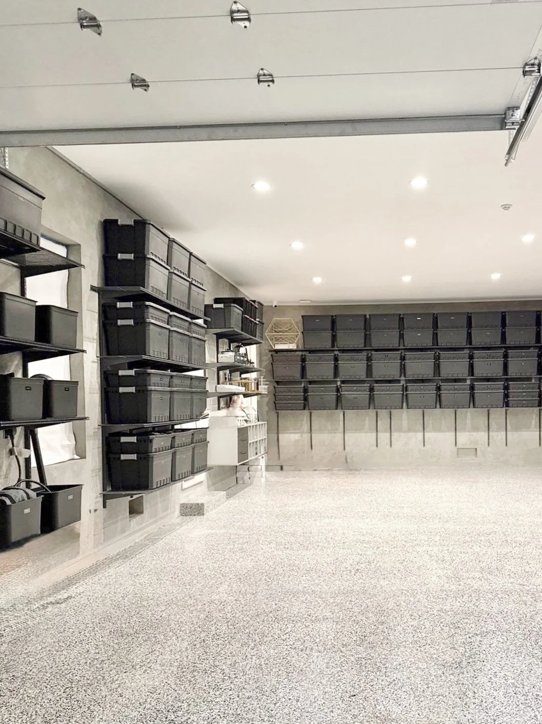 Empty garage with black storage bins on shelves and wall-mounted racks.