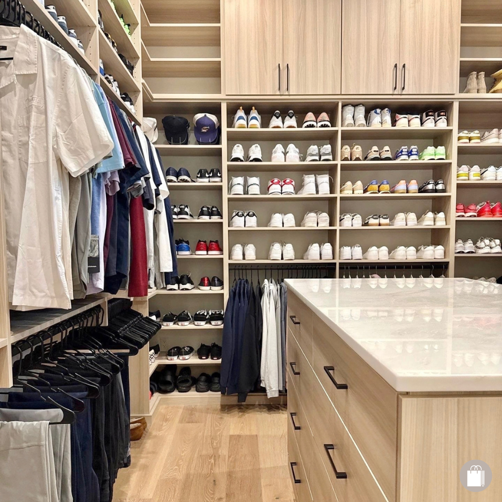 Neatly organized primary closet with hanging clothes, organized shoes on open shelving, and island dresser.