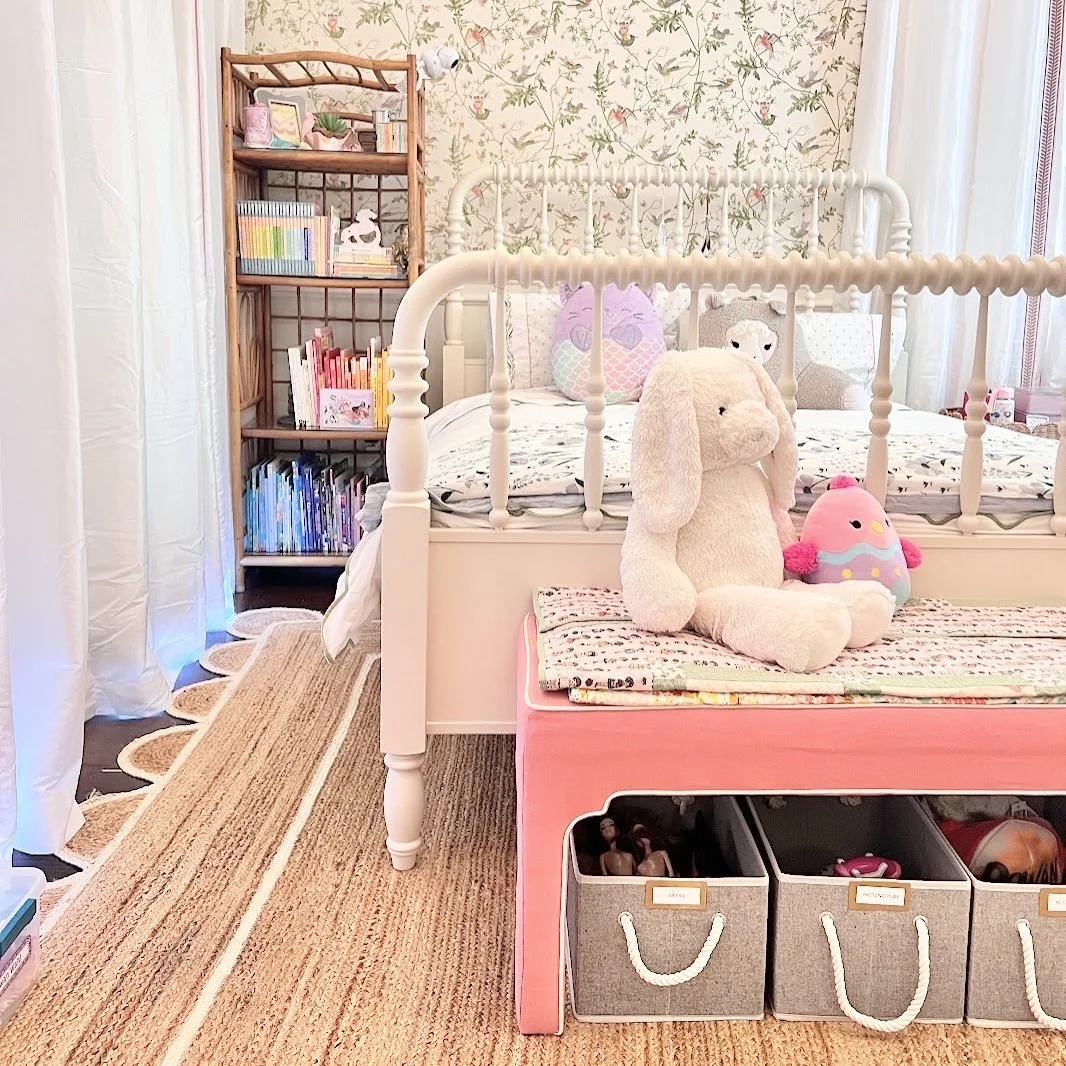 Young girl's bedroom with a pink bench, stuffed animals, labeled rope-handle bins, and a wooden bookcase filled with organized books, decluttered by Sorted Professional Organizing in New Orleans.