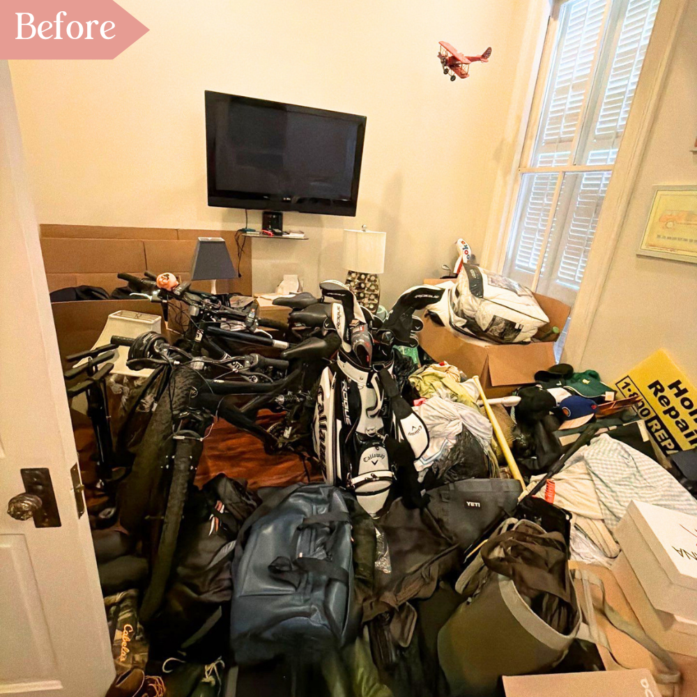 Cluttered before image showing bikes, golf clubs, boxes, books, signs, cardboard, lamps, beneath a wall mounted television and hanging model plane.