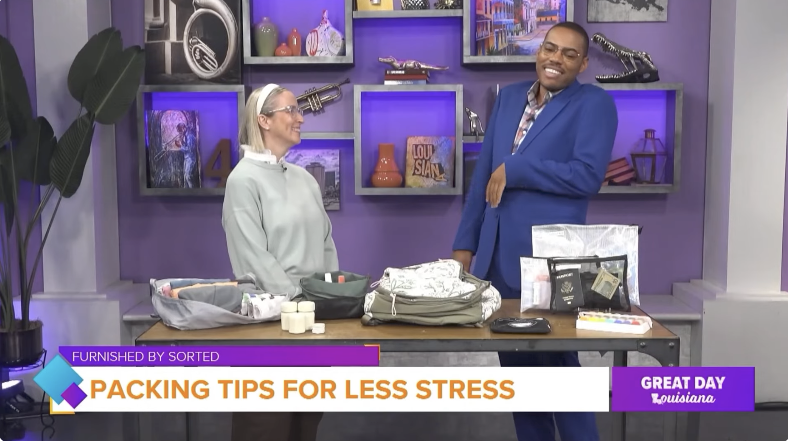 Screenshot of Sorted Founder Victoria Tran in grey sweatshirt and white headband shares Packing Tips for Less Stress while traveling displaying packing cubes, containers, and bags with WWL Great Day Louisiana host Malik Mingo in blue blazer.