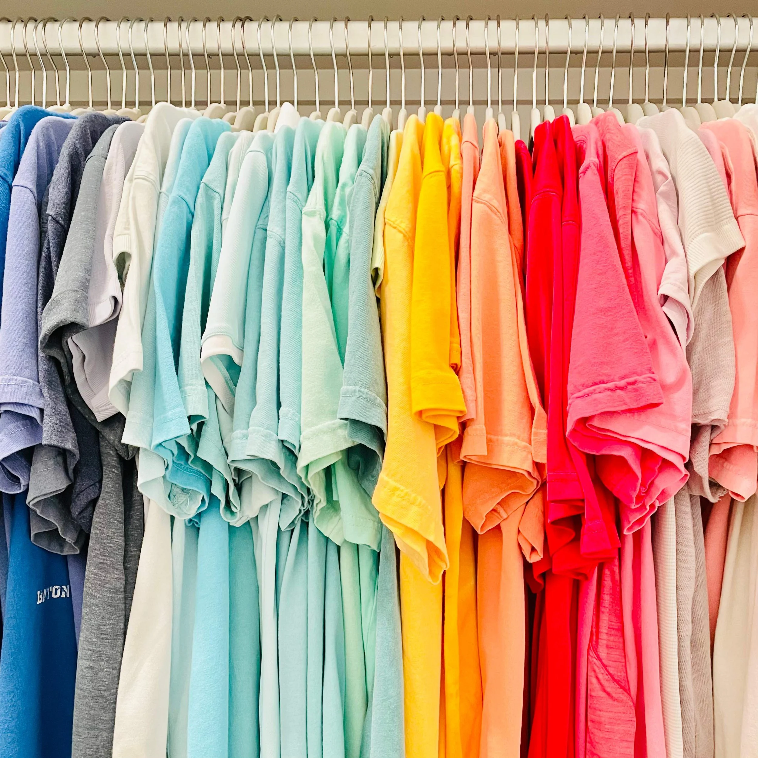 T-shirts hanging on Amazon ivory velvet hangers arranged in rainbow color order.