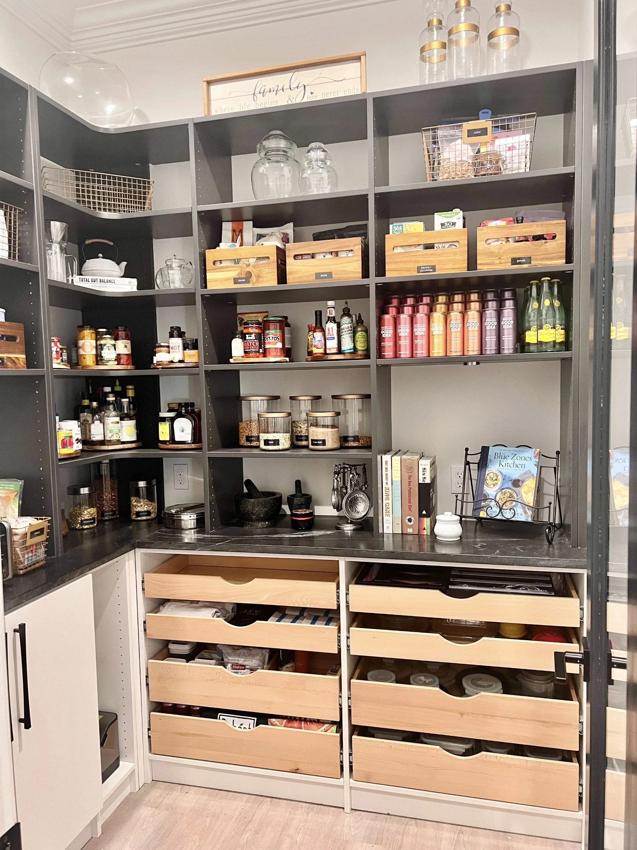 Pantry shelves with various jars, bottles, and boxes of food and spices, with wooden drawers containing pantry items at the bottom, and decorative frames and jars on the top.