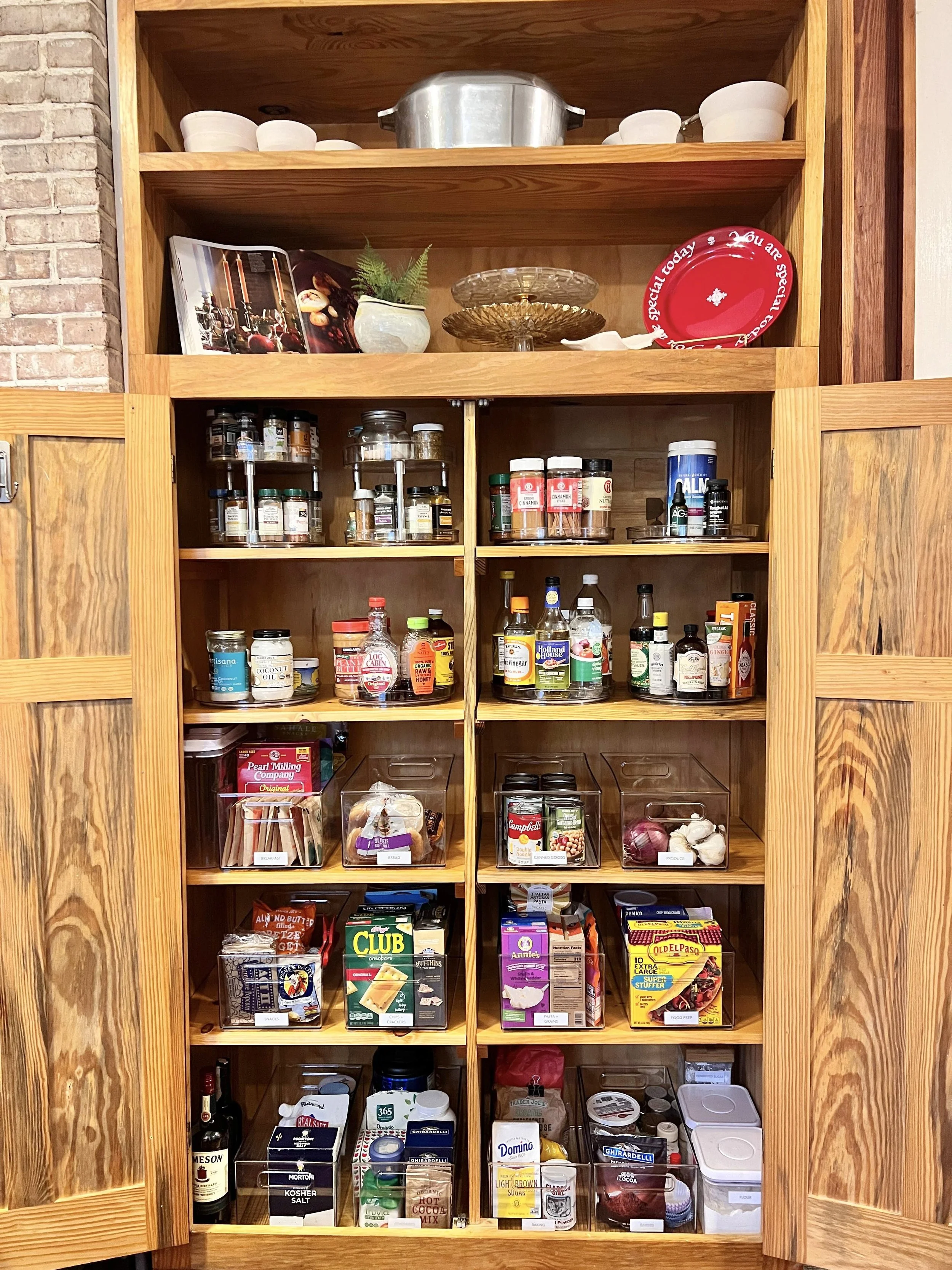 Open wooden cabinet with spices, canned foods, and pantry items on shelves, above a lower section of the cabinet.