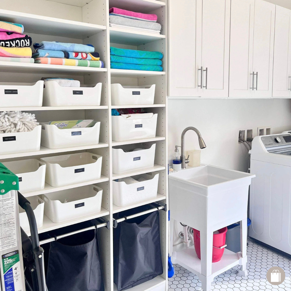 Laundry room with shelves holding folded towels, storage bins, and cleaning supplies, with a laundry sink and washing machine.