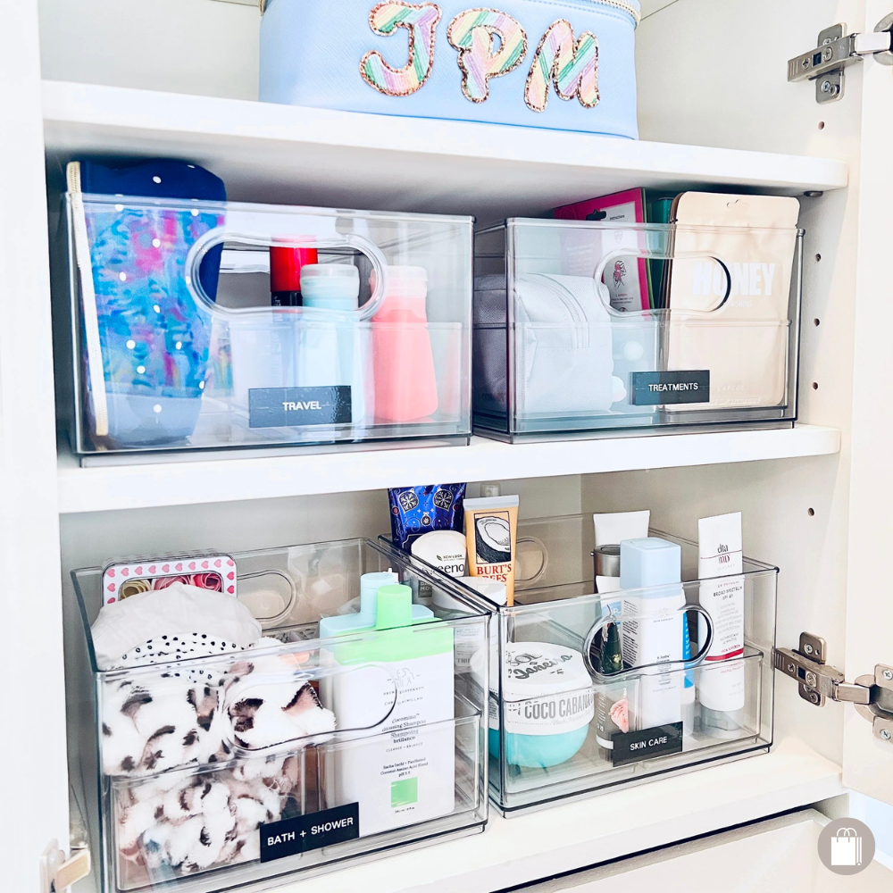 Bathroom cabinet efficiently organized with The Home Edit acrylic bins and labeled for easy access, organized by Sorted Professional Organizing in New Orleans.