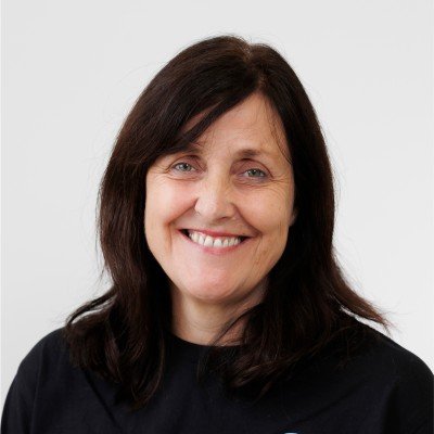 A woman with dark brown hair smiling, wearing a black top, against a light gray background.
