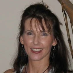 A woman with dark hair and bangs smiling, indoors with a staircase in the background.