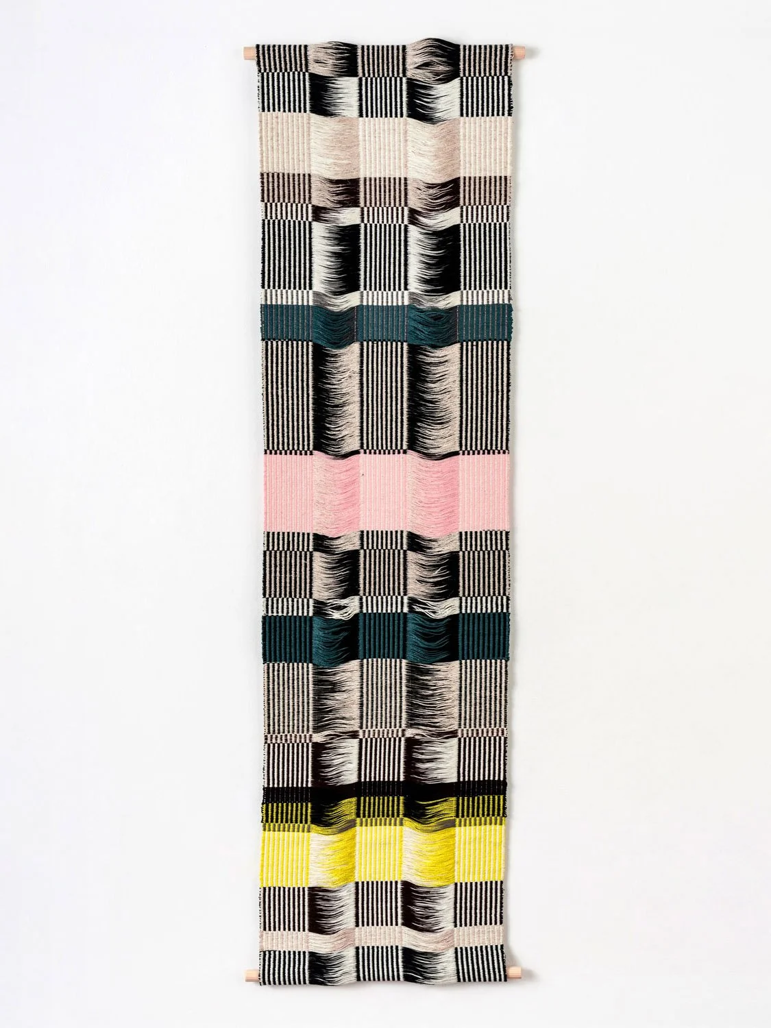 Vertical wall hanging with geometric woven pattern, featuring stripes and blocks in black, white, pink, blue, and yellow.