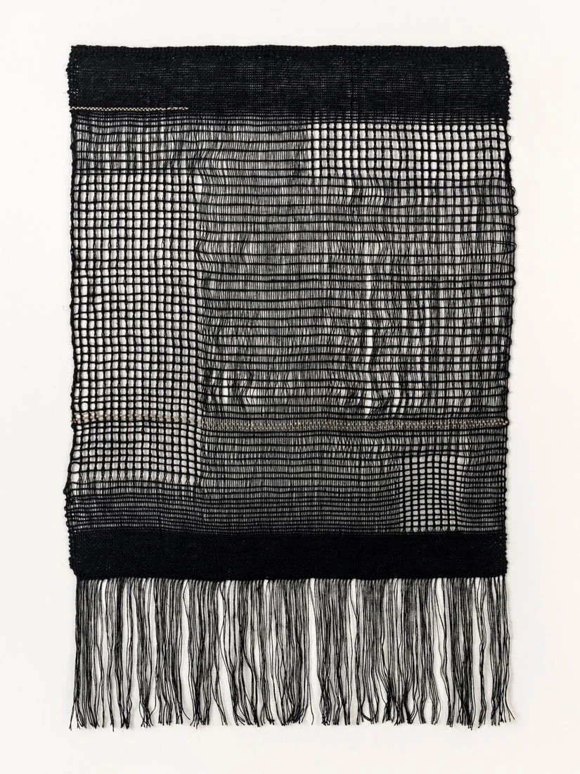 A black woven textile artwork with an open grid pattern, featuring horizontal and vertical lines, with fringes at the bottom.