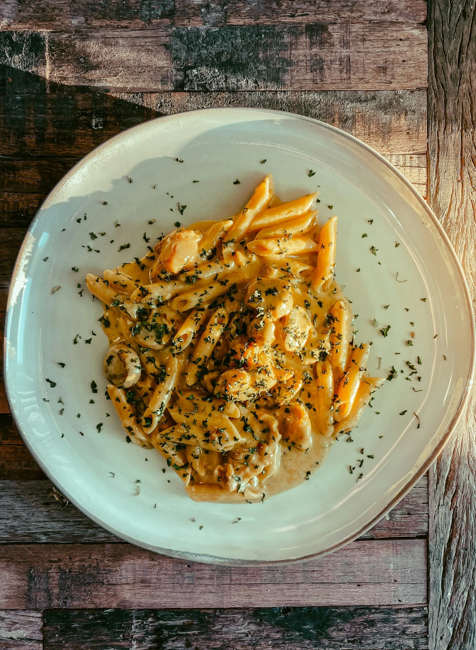 A white plate with pasta covered in creamy sauce and garnished with chopped herbs, placed on a wooden table.