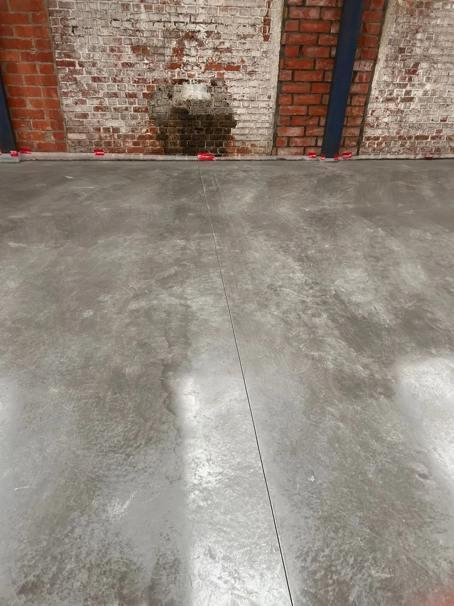 Een muur met bakstenen en cementsporen, en een net geegaliseerde betonnen vloer.