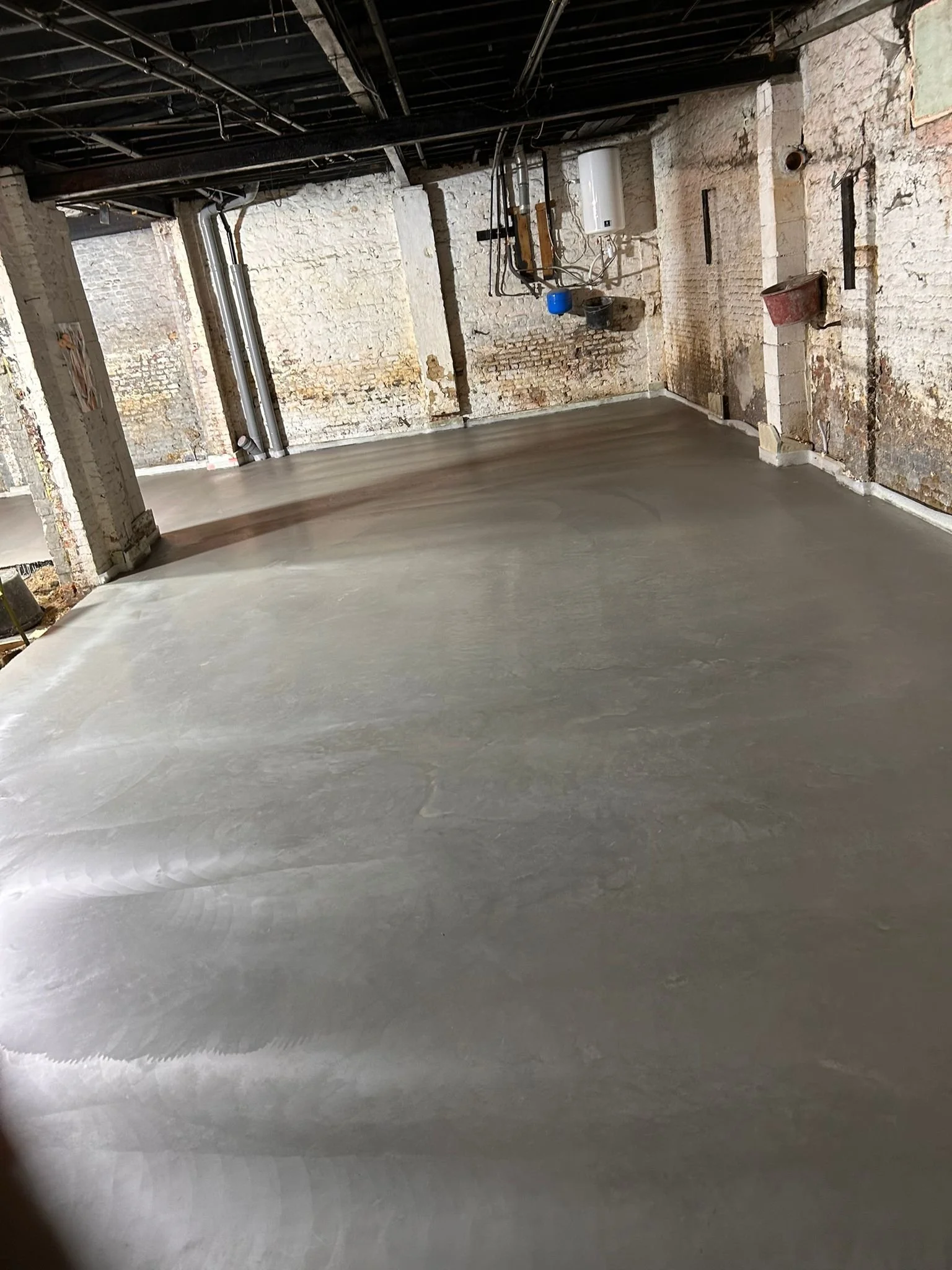 Een kamer met afgewerkte betonnen vloer en ruwe, oude bakstenen muren, waarschijnlijk in een gebouw dat wordt gerenoveerd.