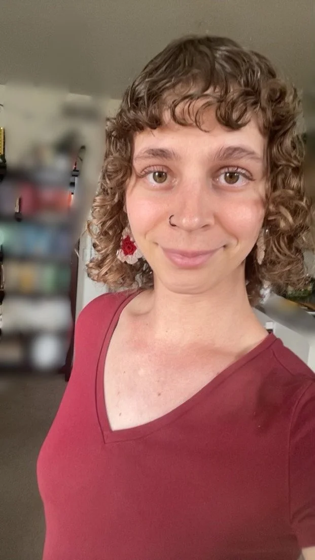 A woman with curly hair and a nose ring smiling while wearing a red shirt.