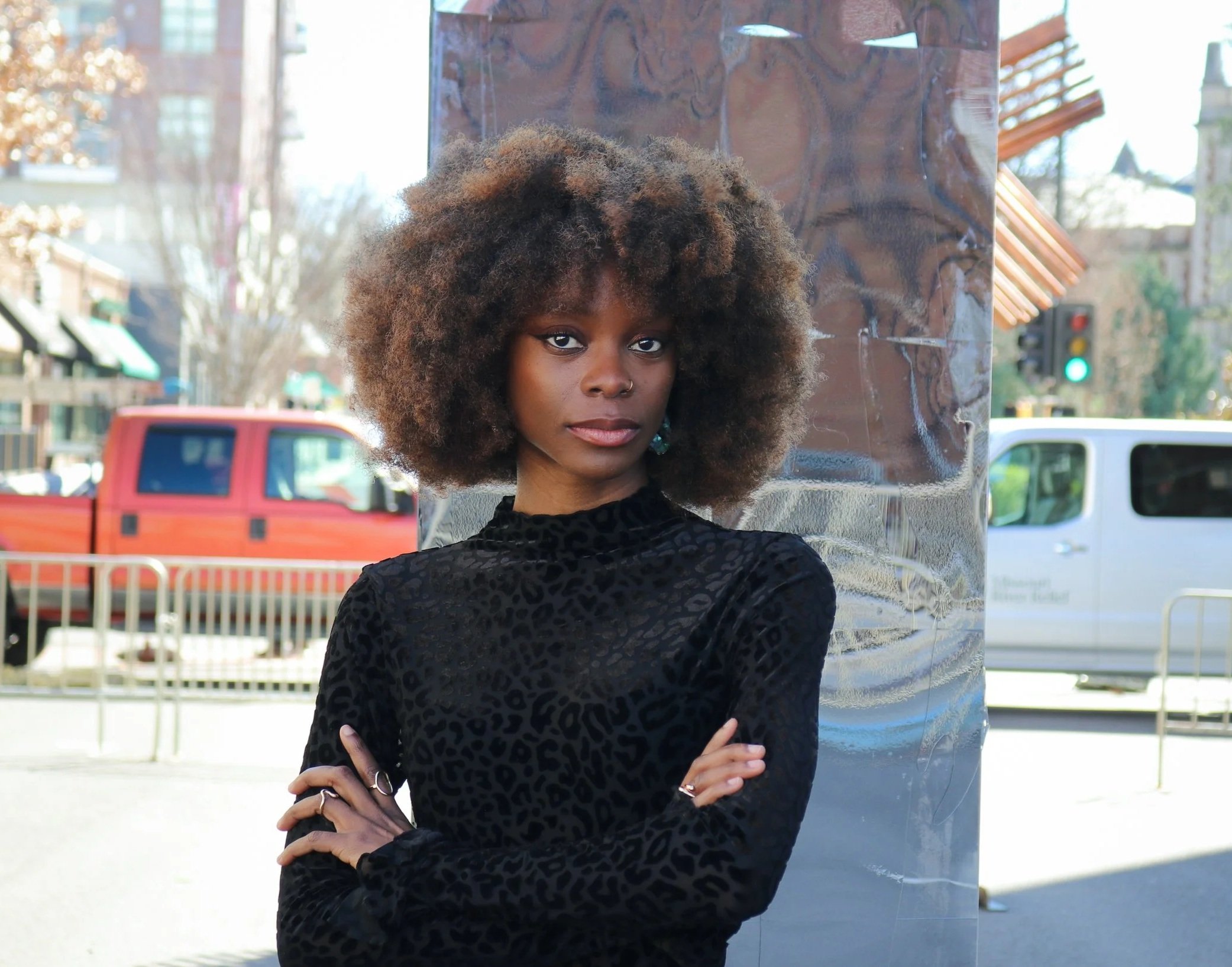 Ayotola Tehingbola is wearing a black shirt and posing in front of a reflective surface...
