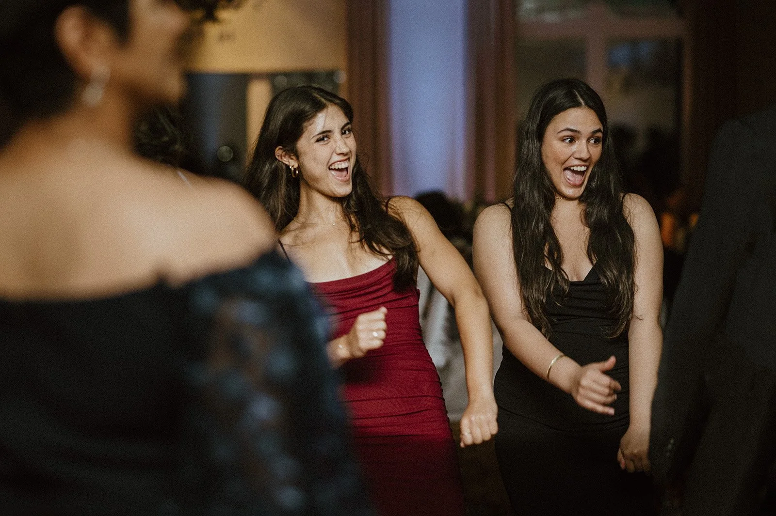 Two women dancing at a small wedding in toronto, smiling and having fun, in elegant dresses.