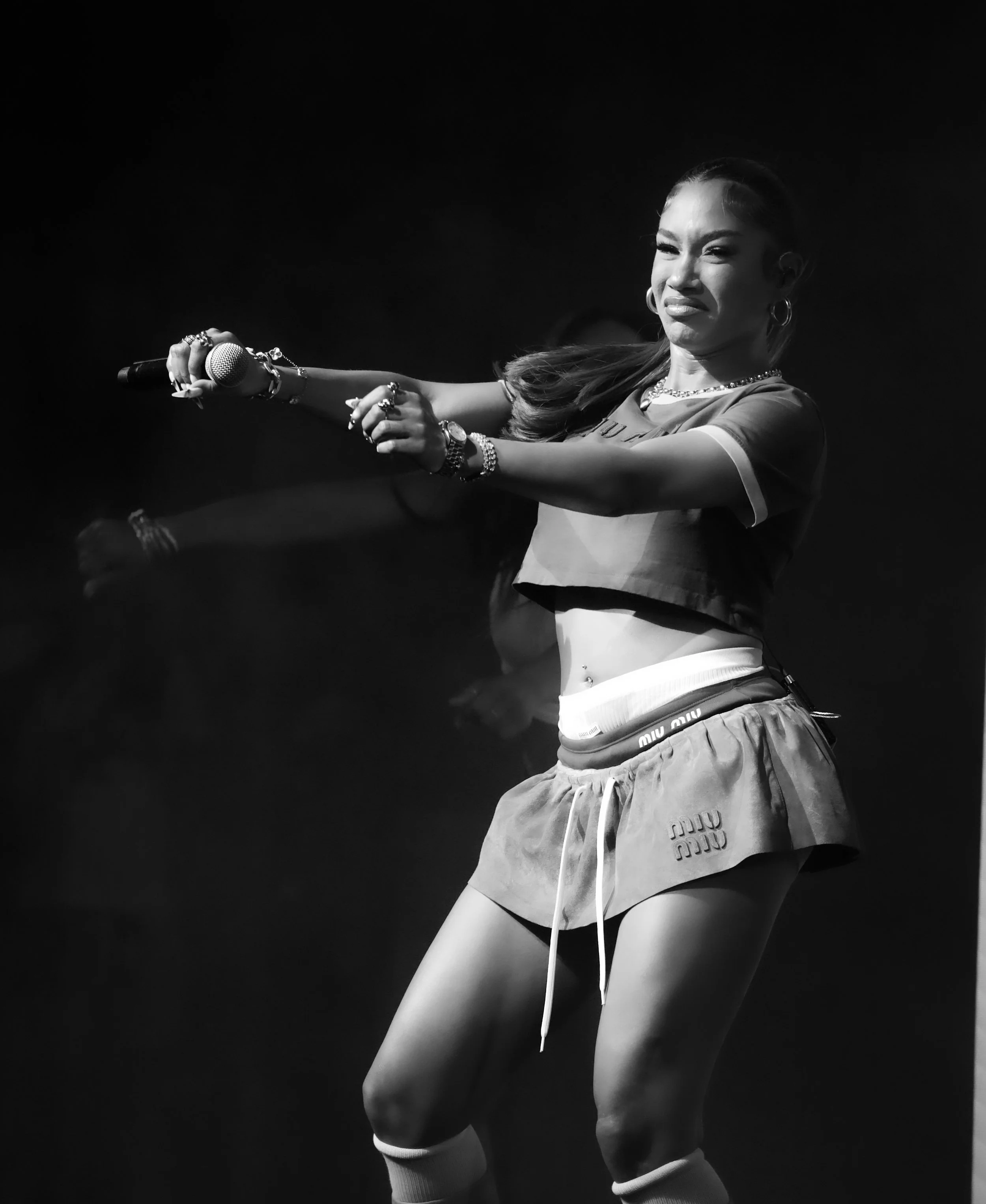 A woman performing on stage, holding a microphone, in athletic clothing, in black and white.