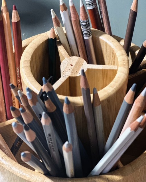 A wooden container holding colored pencils with a segmented inner divider.